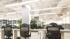 Ein minimalistisches Bürodesign mit weißen Tischen, schwarzen Bürostühlen und einer klaren, gut beleuchteten Raumgestaltung.