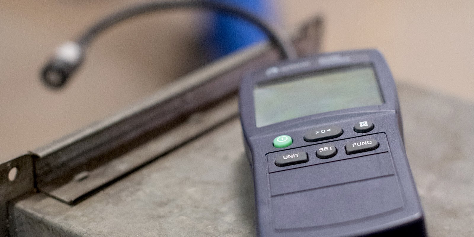 Nahaufnahme eines Messgeräts mit einem klaren Display und Tasten, das auf einer grauen Metalloberfläche platziert ist.