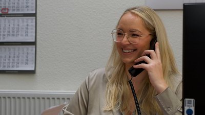 Eine fröhliche Frau telefoniert in einem Büro, ihre langen blonden Haare fallen über die Schultern.