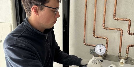 Der Techniker in einem schwarzen Pullover konzentriert sich auf die Druckmessung an einer Heizungsinstallation mit Kupferrohren.