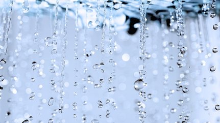 Eine Nahaufnahme von Wasser, das in feinen Strahlen herabfällt, umgeben von einem verschwommenen, glitzernden Hintergrund.