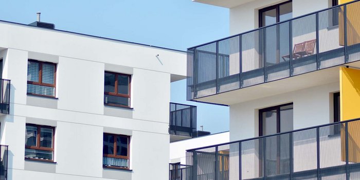 Zwei moderne Wohngebäude mit Balkonen, eines in Weiß und das andere mit einem gelben Akzent, unter einem klaren blauen Himmel.