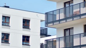 Zwei moderne Wohngebäude mit Balkonen, eines in Weiß und das andere mit einem gelben Akzent, unter einem klaren blauen Himmel.