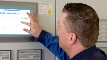 Ein Mann in blauer Arbeitskleidung bedient einen digitalen Bildschirm, während er auf die Anzeige zeigt.