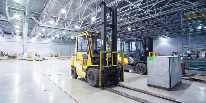 In einem großen Lager stehen zwei Gabelstapler, einer gelb und einer schwarz, bereit für den Einsatz zwischen Paletten.