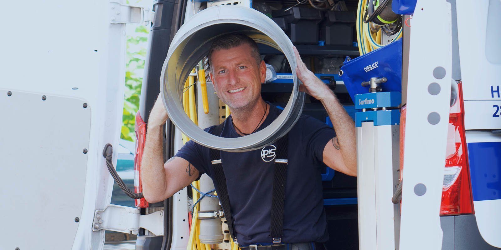 Der Mann in Arbeitskleidung zeigt stolz einen großen Rohrabschnitt, während er in einem gut organisierten Lieferwagen steht.