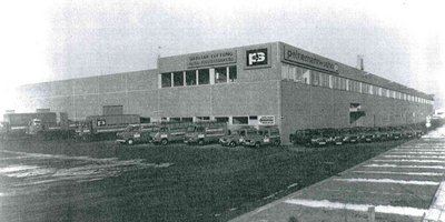 Ein großes Industriegebäude mit mehreren Lkw und Lieferwagen, die ordentlich auf dem Parkplatz geparkt sind.