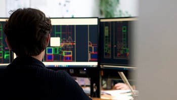 In einem modernen Büro arbeitet ein Mann an Computerbildschirmen, die komplexe Entwürfe und Pläne darstellen.