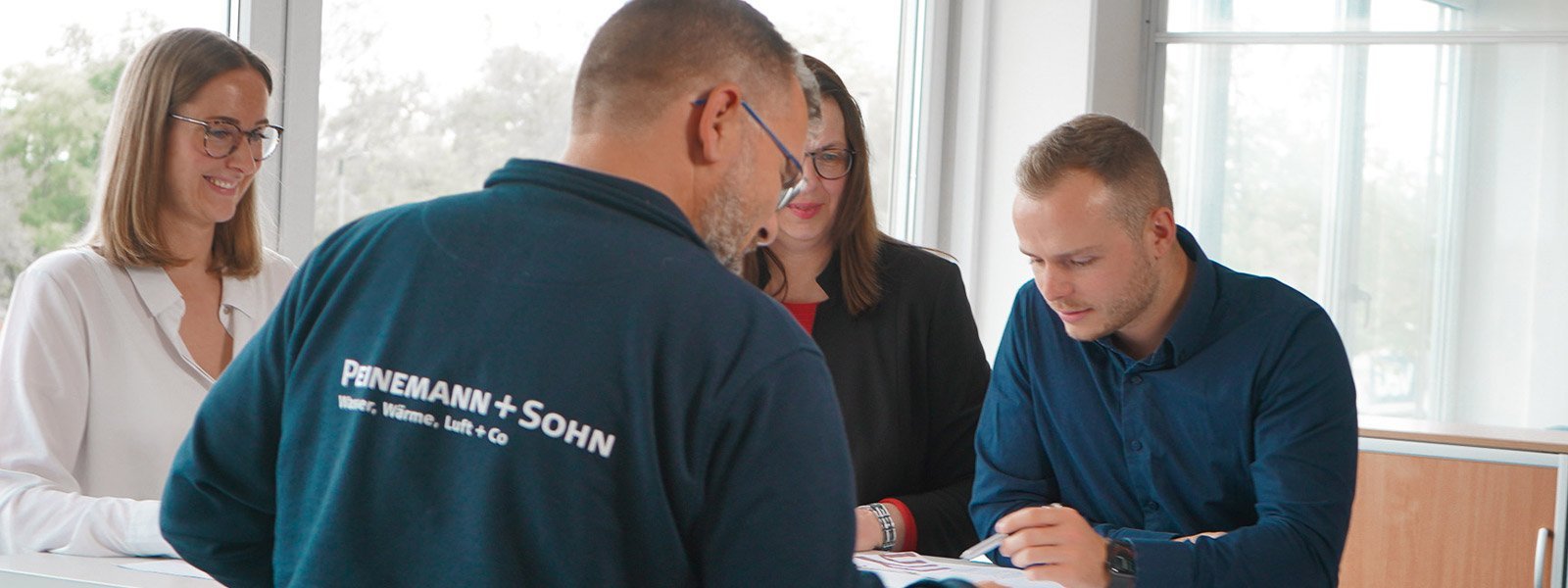 In einem lichtdurchfluteten Raum arbeiten vier Personen zusammen, während sie Dokumente und Notizen durchsehen.