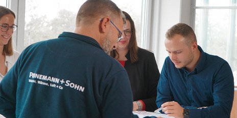 In einem lichtdurchfluteten Raum arbeiten vier Personen zusammen, während sie Dokumente und Notizen durchsehen.