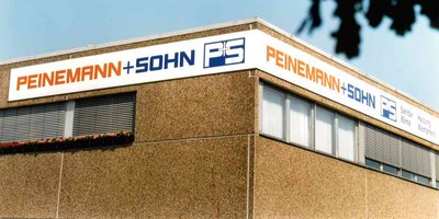 Das Gebäude zeigt ein großes Schild mit dem Namen 'PEINEMANN + SOHN' in orange und blau, umgeben von einem klaren Himmel.