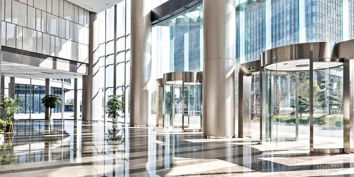 Ein heller, moderner Eingangsbereich mit großen Fenstern und glänzendem Boden, umgeben von Pflanzen und Glastüren.