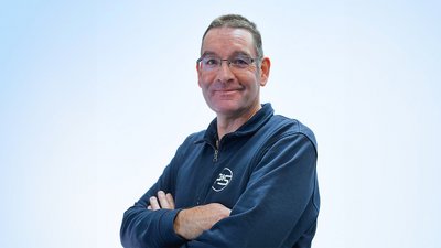 Der Mann trägt einen blauen Pullover und hat einen selbstbewussten Ausdruck, der eine positive Ausstrahlung vermittelt.