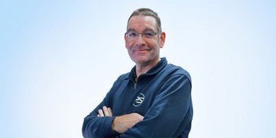 Der Mann trägt einen blauen Pullover und hat einen selbstbewussten Ausdruck, der eine positive Ausstrahlung vermittelt.