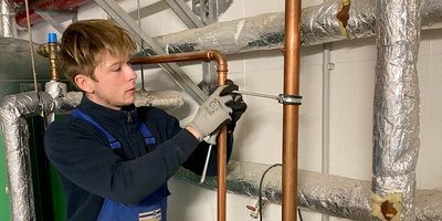 Ein junger Handwerker arbeitet konzentriert an einer Kupferrohrinstallation in einem technischen Raum.