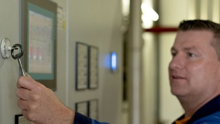 Ein Mann benutzt einen Schlüssel, um ein Gerät an einer Wand zu öffnen, während er auf einen Bildschirm schaut.