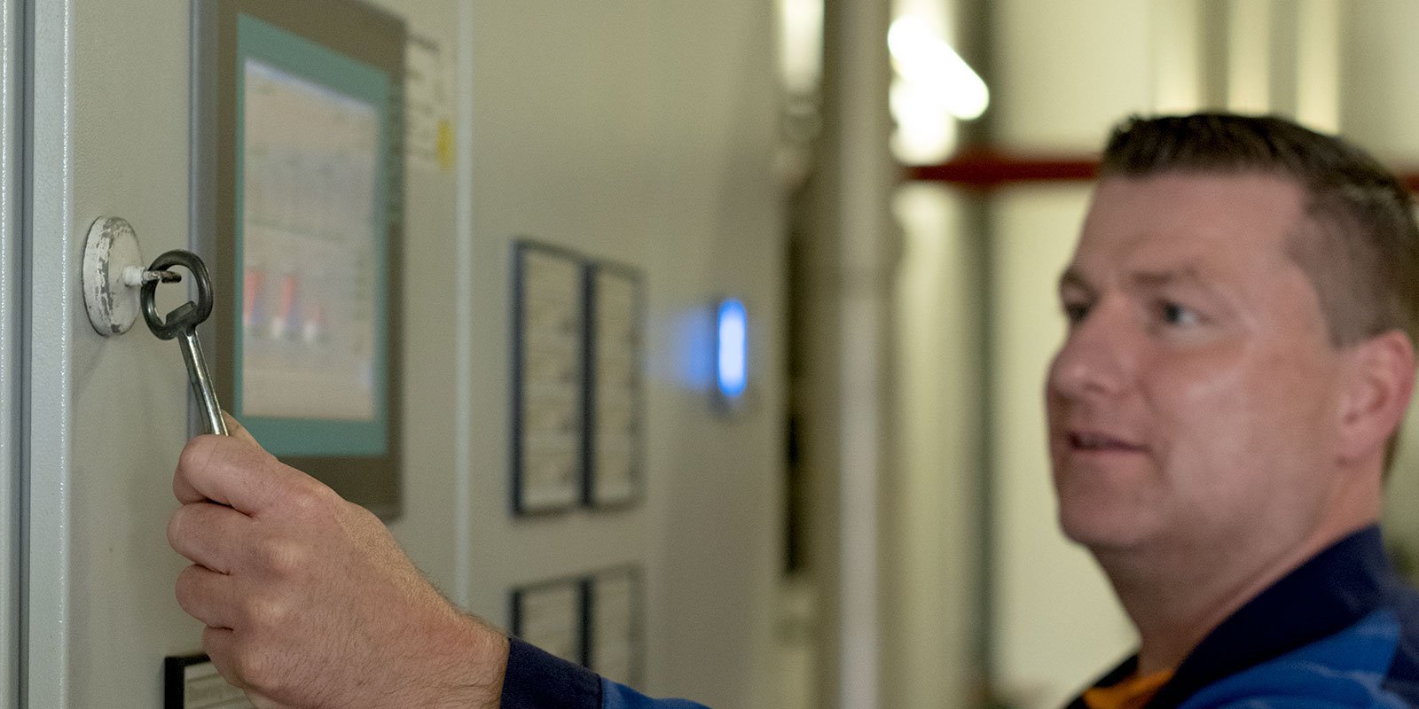 Ein Mann benutzt einen Schlüssel, um ein Gerät an einer Wand zu öffnen, während er auf einen Bildschirm schaut.