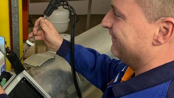 Ein Techniker arbeitet konzentriert an einem Gerät, während er ein Werkzeug in der Hand hält und lächelt.