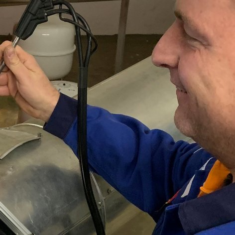 Ein Techniker arbeitet konzentriert an einem Gerät, während er ein Werkzeug in der Hand hält und lächelt.