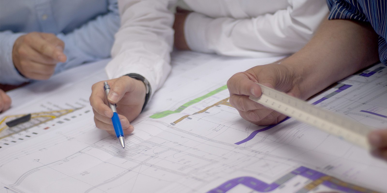 Hände von Fachleuten, die einen Plan analysieren, während sie wichtige Details mit einem Stift markieren.