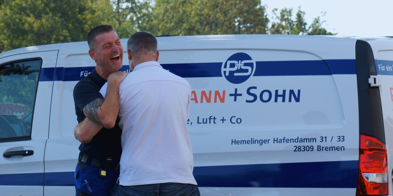 Zwei Männer umarmen sich herzlich vor einem Lieferwagen, während sie fröhlich lachen und eine freundliche Atmosphäre ausstrahlen.