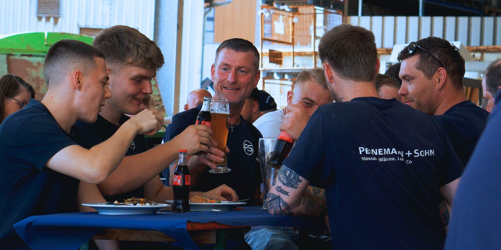 Eine Gruppe von Männern hebt ihre Gläser in einem fröhlichen Trinkspruch, während sie an einem Tisch mit Essen sitzen.