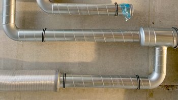 Eine Anordnung von silbernen Rohren, die sich in verschiedenen Richtungen winden und an einer Wand befestigt sind.