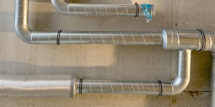 Eine Anordnung von silbernen Rohren, die sich in verschiedenen Richtungen winden und an einer Wand befestigt sind.