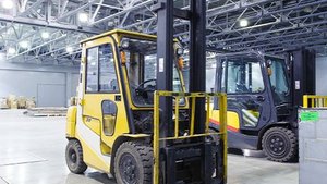 Ein gelber Gabelstapler steht in einer großen Lagerhalle, umgeben von anderen Maschinen und Regalen voller Waren.